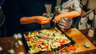 Young boy sprinkling fresh herbs on vegetable dish